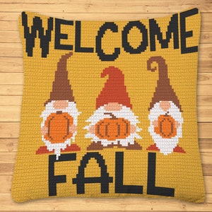 May include: Mustard yellow pillow with the words "WELCOME FALL" in black pixelated letters. Three gnomes with orange pumpkins, brown and red hats, and white beards are featured on the pillow.