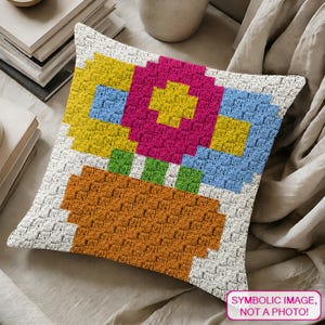 May include: A square, crocheted pillow with a colorful floral design. The flowers are pink, yellow, and blue, with green stems, in an orange pot. The pillow has a white border and the text "SYMBOLIC IMAGE, NOT A PHOTO!"