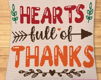 Peut inclure: Un coussin en crochet beige avec le texte "HEARTS full of THANKS" en fil brun, rouge et orange. Le coussin a une flèche brune pointant vers la droite et un petit cœur au milieu du texte. Le coussin est décoré de feuilles brunes et d'un petit cœur en bas.