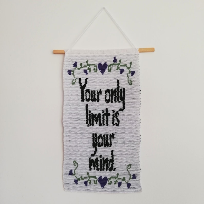 Pu&ograve; includere: Arazzo da parete in crochet bianco con il testo "Your only limit is your mind." in lettere nere. L'arazzo &egrave; decorato con un tralcio di foglie verdi e cuori viola.