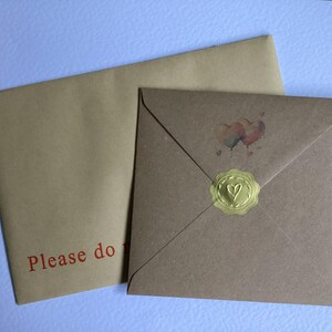 May include: Two brown envelopes, one on top of the other. The top envelope has a gold wax seal with a heart design. The bottom envelope has the text "Please do" printed in red.