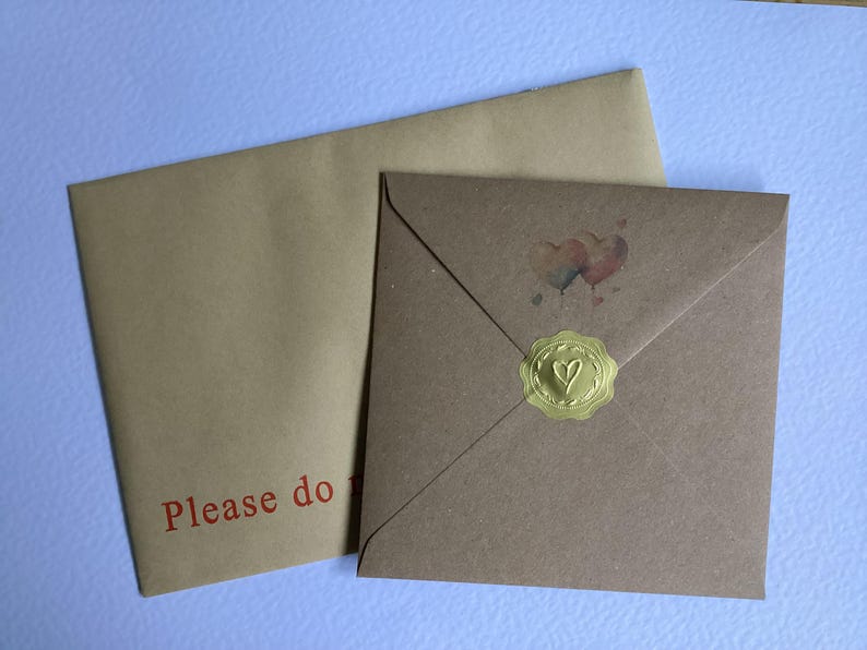 May include: Two brown envelopes, one on top of the other. The top envelope has a gold wax seal with a heart design. The bottom envelope has the text "Please do" printed in red.