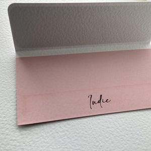 K&ouml;nnte beinhalten: Ein rosa Umschlag mit dem Wort "Indie" in schwarzer Tinte.