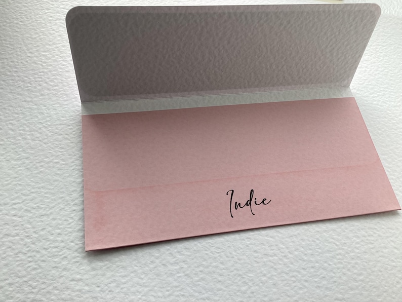 K&ouml;nnte beinhalten: Ein rosa Umschlag mit dem Wort "Indie" in schwarzer Tinte.
