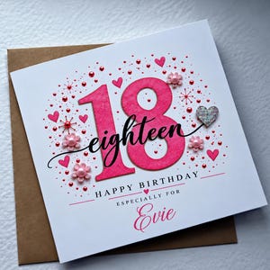 May include: A square white birthday card featuring a large pink glittery number 18, the word eighteen in black script, and the text HAPPY BIRTHDAY ESPECIALLY FOR Evie. The design includes pink hearts, small pearls, and floral accents.