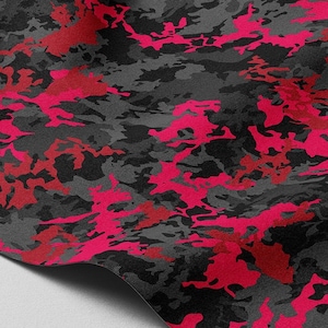 Puede incluir: Primer plano de una tela de camuflaje rosa y negro. La tela está doblada y tiene una superficie suave y texturizada.