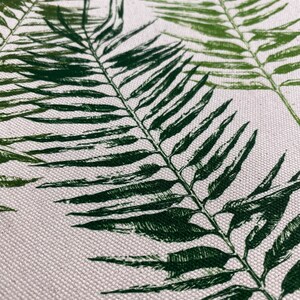 May include: Close-up of a white fabric with a green fern leaf pattern. The fabric has a textured surface.