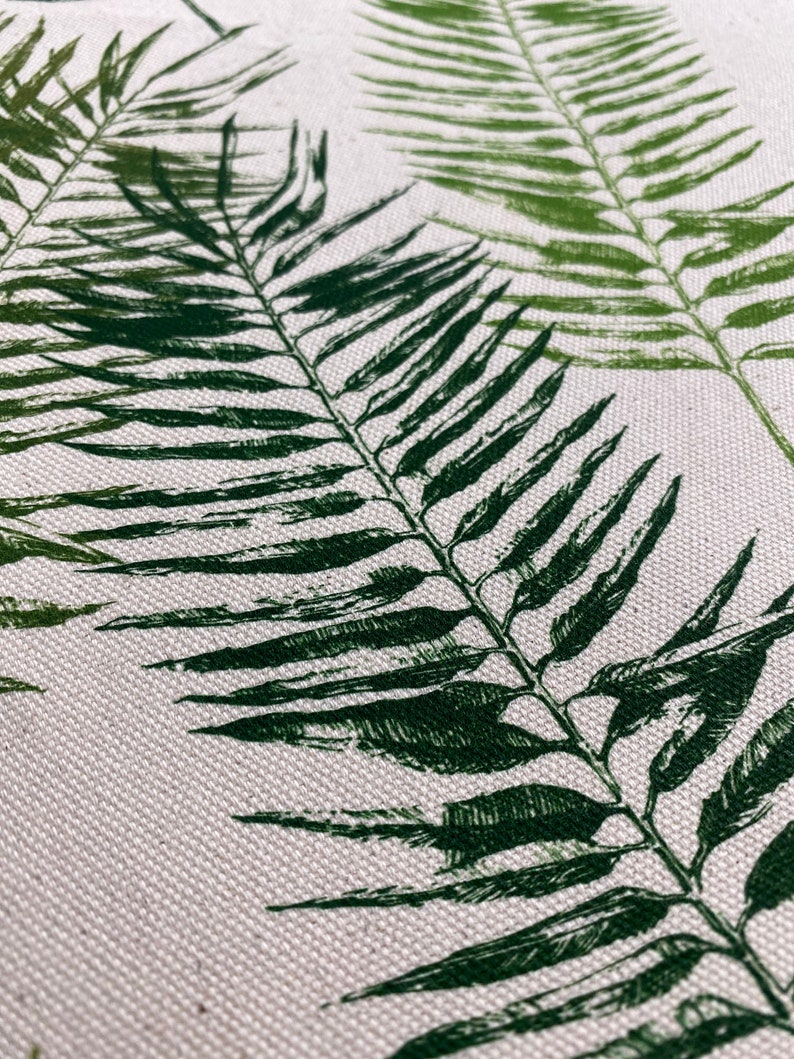 May include: Close-up of a white fabric with a green fern leaf pattern. The fabric has a textured surface.