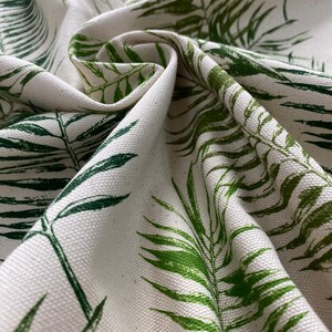 May include: White fabric with a green leafy pattern. The fabric is folded and shows the texture of the material.