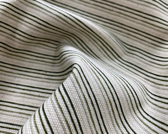 May include: Close-up of a white fabric with thin green stripes. The fabric is wrinkled and has a textured surface.