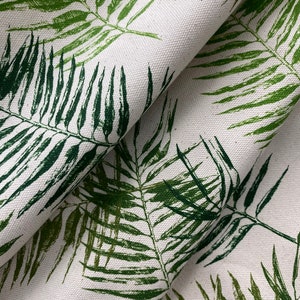 May include: Close-up of a white fabric with a green leafy pattern. The fabric is folded and the leaves are printed in a dark green color.