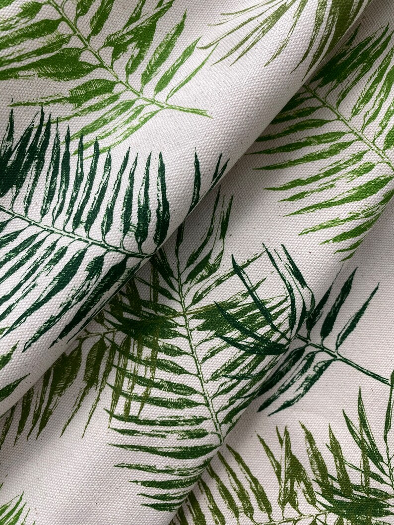 May include: Close-up of a white fabric with a green leafy pattern. The fabric is folded and the leaves are printed in a dark green color.