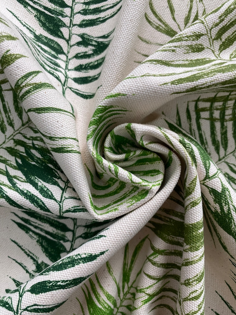 May include: Close-up of a white fabric with a green leafy pattern. The fabric is folded and textured, showing the detail of the print.