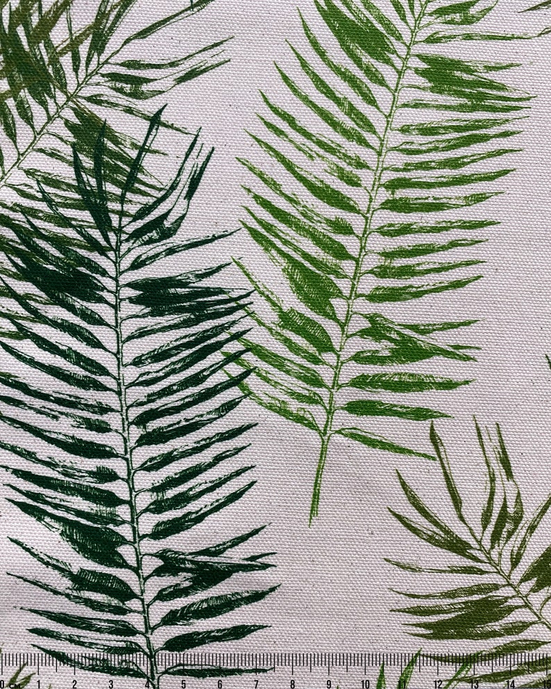 May include: A white fabric with a repeating pattern of green palm leaves. The fabric is measured with a ruler in inches.