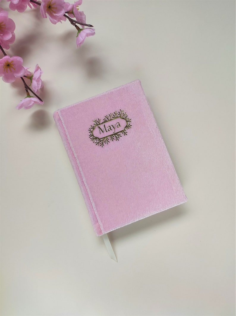 May include: A pink velvet journal with a gold bookmark and the name "Maya" embossed on the front cover.