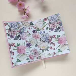 May include: Pink velvet journal with a floral pattern on the inside pages. The pattern features pink, white, and purple flowers.