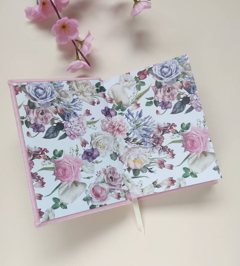 May include: Pink velvet journal with a floral pattern on the inside pages. The pattern features pink, white, and purple flowers.