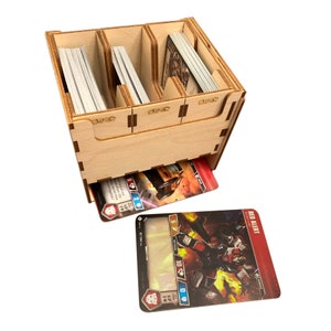 Op de afbeelding: Een houten kaartspelorganizer met vier compartimenten om kaarten op te bergen. De organizer heeft een uittrekbare lade voor gemakkelijke toegang tot kaarten. De organizer is gemaakt van licht hout en heeft een natuurlijke afwerking.