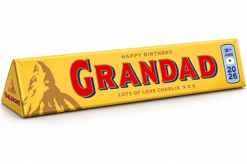 Pu&ograve; includere: Una barretta di cioccolato Toblerone triangolare in confezione gialla con il testo HAPPY BIRTHDAY GRANDAD LOTS OF LOVE CHARLIE X X X. Il lato mostra un grafico di montagna marrone e la data 18TH JUNE 2026 in un riquadro blu.