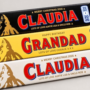 Pu&ograve; includere: Tre barrette di cioccolato Toblerone triangolari con confezioni personalizzate. La barretta superiore &egrave; nera con 'CLAUDIA', quella centrale &egrave; gialla con 'GRANDAD' e quella inferiore &egrave; bianca con 'CLAUDIA'. Ognuna presenta il logo della montagna.