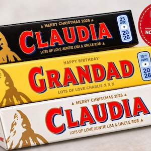 May include: Three triangular candy bar wrappers featuring custom text. The top is black with 'CLAUDIA', the middle is yellow with 'GRANDAD', and the bottom is white with 'CLAUDIA'. Each includes dates, the Toblerone logo, and a red 'LABEL ONLY' circle.