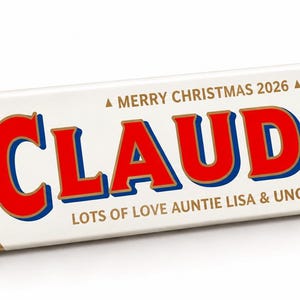 Pu&ograve; includere: Una confezione triangolare bianca di cioccolato Toblerone con il nome CLAUDIA in grandi lettere rosse. Il testo recita MERRY CHRISTMAS 2026, LOTS OF LOVE AUNTIE LISA & UNCLE ROB, e include un'icona di calendario con 25 DEC 2026.