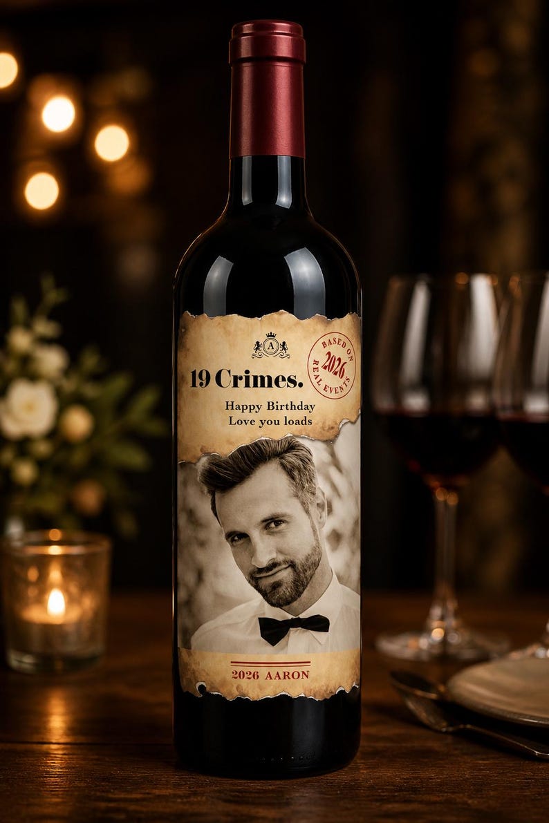 Puede incluir: Botella de vino tinto oscuro con una etiqueta personalizada que presenta un retrato en sepia de un hombre. La etiqueta dice "19 Crimes", "Happy Birthday, Love you loads" y "2026 Aaron". La botella est&aacute; sobre una superficie de madera.