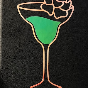 May include: A black leather-bound book with the title "Courtney's Cocktails" in pink script. A stylized illustration of a martini glass with a green liquid and a rose on top is above the title.