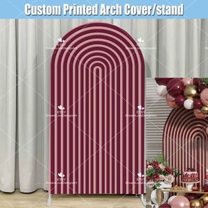 May include: A burgundy and blush pink striped arch backdrop for a party or event. The backdrop is made of cardboard and is freestanding. The backdrop is decorated with balloons and a table with a cake and other decorations.
