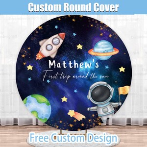 May include: A round, blue and purple space-themed backdrop with stars, planets, a rocket ship, and an astronaut. The text "Matthew's First trip around the sun" is written in white.