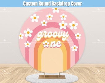 May include: A pink and orange round backdrop with a rainbow design and white daisies. The text "groovy*one" is written in a retro font.