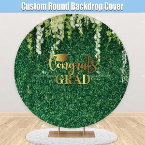 May include: A round backdrop cover with a green hedge background, white flowers, and the gold text "Congrats Grad" with a graduation cap. The backdrop is on a gold stand and a white rug.