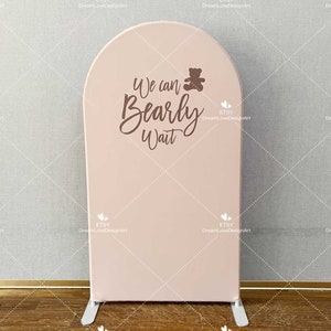 May include: A pink archway backdrop with the text "We can Bearly Wait" in brown script. A small brown teddy bear icon is above the text.