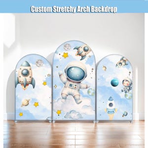 Puede incluir: Fondo de arco elástico personalizado con tres paneles con temática espacial. Cada panel muestra cohetes, planetas, estrellas y un astronauta sobre un fondo de cielo azul claro. El texto "Custom Stretchy Arch Backdrop" está en la parte superior.