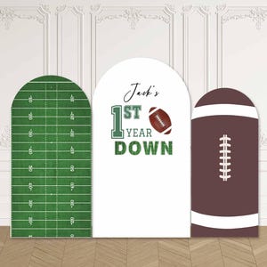 Può includere: Tre pannelli ad arco a tema football americano. Un pannello è un campo da football verde, un altro ha il testo "Jack's 1st Year Down" con una grafica di pallone da football, e il terzo è un pallone da football marrone.