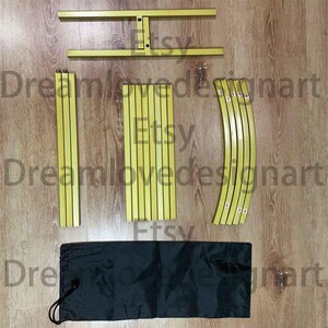 May include: Yellow metal frame components, including straight and curved pieces, and a black drawstring bag, are arranged on a wooden surface. The components appear to be for a display or backdrop structure.