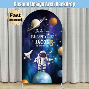 May include: A blue and purple space-themed arch backdrop with a white astronaut, planets, and stars. The text reads "3, 2, 1... BLAST OFF! JACOB 5 is turning".