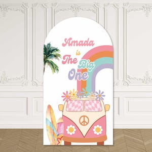 May include: A white arch-shaped sign with a retro design. The sign features a pink and orange van with a peace sign, a rainbow, and the text "Amada is The Big One." A palm tree and a surfboard are also included.
