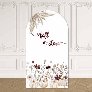 Op de afbeelding: Een boogvormige achtergrond met de tekst fall in Love in donkerrood handschrift. De linkerbovenhoek bevat een bosje gedroogd pampasgras. Het onderste gedeelte toont een aquarelillustratie van witte pompoenen en diverse wilde bloemen in zachte tinten.