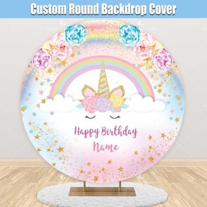 May include: A round pink and blue backdrop with a rainbow, clouds, gold glitter, and stars. A unicorn head with a flower crown is in the centre. The text "Happy Birthday Name" is below the unicorn.