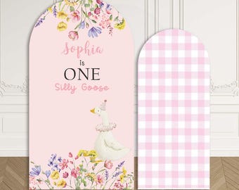 May include: A custom stretchy arch backdrop with a pink background. The left arch features the text "Sophia is ONE Silly Goose" with a goose illustration and floral accents. The right arch has a pink and white gingham pattern.