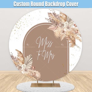 May include: A round backdrop with a white background and a brown archway with the text "Miss to Mrs" in white. The archway is decorated with beige and brown dried floral arrangements.