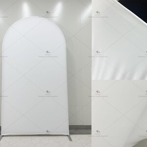 May include: A white arched backdrop with a metal base. The backdrop is made of a smooth, wrinkle-resistant fabric. The fabric is being held up by a person's hand in the upper right corner of the image. The backdrop is designed for events.
