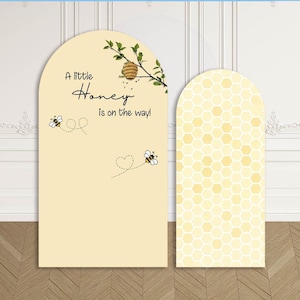 Può includere: Due pannelli espositivi ad arco. Il pannello sinistro è color crema con un alveare, due api e il testo A little Honey is on the way! Il pannello destro presenta un motivo esagonale giallo e bianco ripetuto su tutta la superficie.