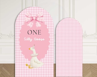 May include: Two arched fabric backdrops featuring a pink and white gingham pattern. The larger backdrop displays a pink scalloped oval with a large pink bow, the text ONE Silly Goose, and a white goose illustration wearing a party hat and ruff.