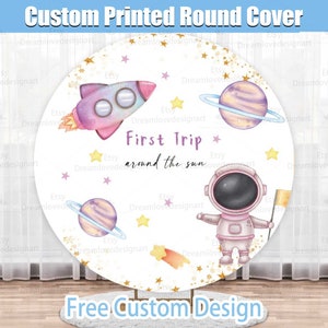 May include: A custom-printed round cover featuring a space-themed design. The design includes a pink rocket, planets with rings, an astronaut, stars, and the text "First Trip around the sun". The cover is white with a light blue border.