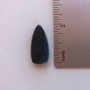 May include: A dark blue, teardrop-shaped labradorite gemstone with iridescent flashes of color. The gemstone is approximately 1 inch long and is shown next to a ruler.