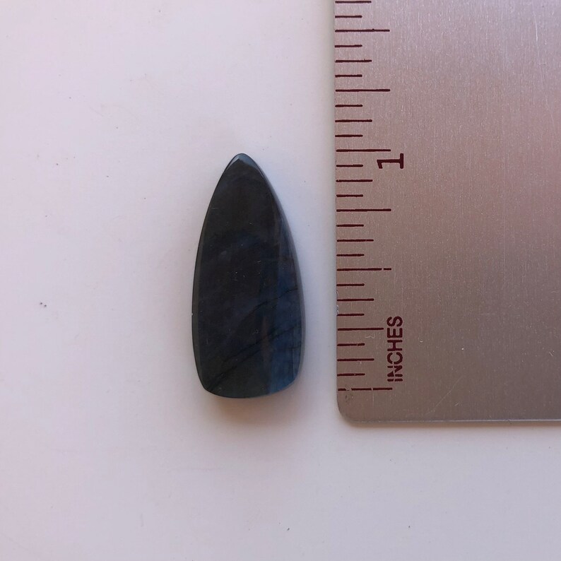 May include: A dark blue, teardrop-shaped labradorite gemstone with iridescent flashes of color. The gemstone is approximately 1 inch long and is shown next to a ruler.