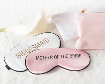 May include: Two satin sleep masks with black trim. One is white with gold lettering that says "BRIDESMAID". The other is pink with black lettering that says "MOTHER OF THE BRIDE".