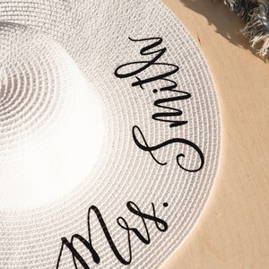 Puede incluir: Sombrero de paja blanco con letras negras en cursiva que dicen "Mrs. Smith"